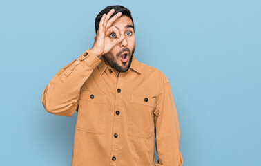 Young hispanic man wearing casual clothes doing ok gesture shocked with surprised face, eye looking through fingers. unbelieving expression.