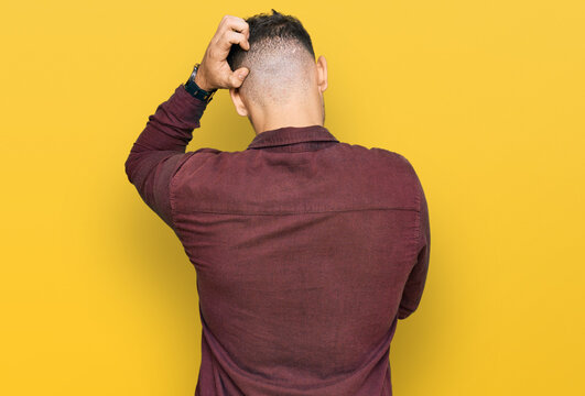Young hispanic man wearing casual clothes backwards thinking about doubt with hand on head