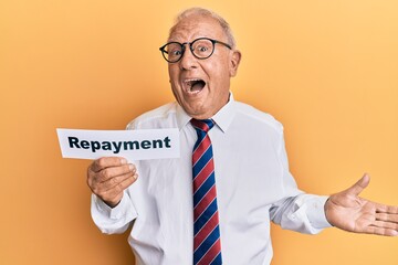 Senior caucasian man holding repayment word paper celebrating achievement with happy smile and winner expression with raised hand