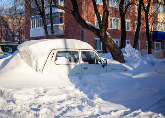 A passenger car in winter was covered with snow after a snow storm.