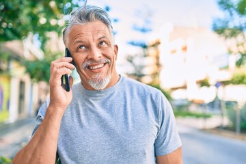 Middle age hispanic grey-haired man smiling happy talking on the smartphone at the city.