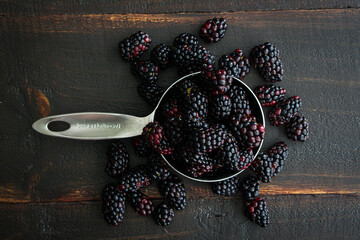 Measuring Cup filled with Fresh Blackberries: A metal measuring cup filled with fresh berries on a wooden table