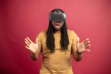 Surprised scared African American mixed-race man with dreadlocks and open mouth isolated over red wall touching air with hands, spending time in virtual reality, playing games in modern VR headset