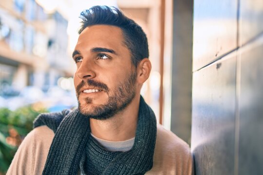Young hispanic man smiling happy wearing scarf leaning on the wall at the city.