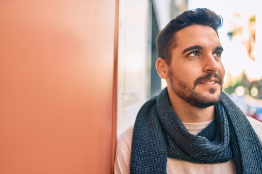 Young hispanic man smiling happy wearing scarf leaning on the wall at the city
