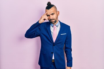 Young hispanic man wearing business suit and tie pointing unhappy to pimple on forehead, ugly infection of blackhead. acne and skin problem