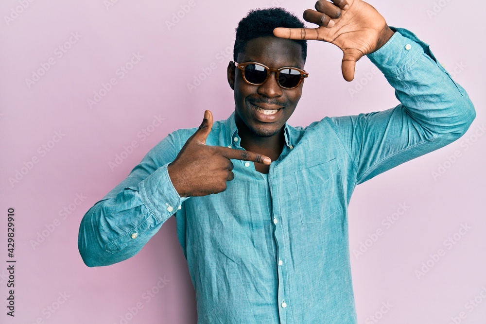 Wall mural Handsome business black man wearing stylish sunglasses smiling making frame with hands and fingers with happy face. creativity and photography concept.