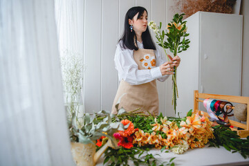 a young brunette woman in an apron in the process of creating a bouquet in the rustic style in her flower shop