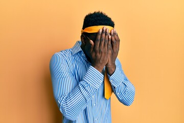 Handsome black man drunk wearing tie over head and sunglasses with sad expression covering face with hands while crying. depression concept.