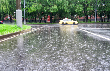 Heavy rain with hail in the city on a summer day. Large puddles on the roadway. Wet road with puddles of spray.