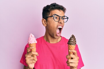 Young handsome african american man holding ice cream cones angry and mad screaming frustrated and...