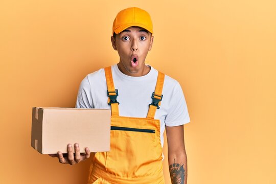 Young handsome african american man holding delivery package scared and amazed with open mouth for surprise, disbelief face