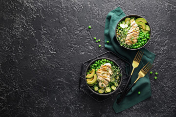 Bowls of tasty salad with fresh vegetables and chicken on dark background