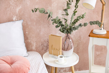 Bedside table with vase and cup of coffee near color wall in room