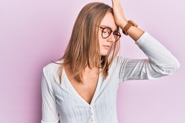 Beautiful blonde woman wearing casual clothes and glasses surprised with hand on head for mistake,...