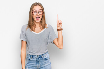 Beautiful young blonde woman wearing casual clothes and glasses pointing finger up with successful...