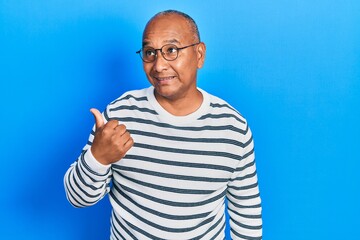 Naklejka premium Middle age latin man wearing casual clothes and glasses smiling with happy face looking and pointing to the side with thumb up.