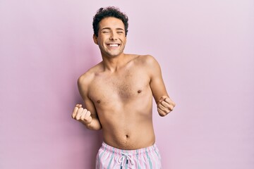 Fototapeta premium Young handsome man wearing swimwear shirtless very happy and excited doing winner gesture with arms raised, smiling and screaming for success. celebration concept.