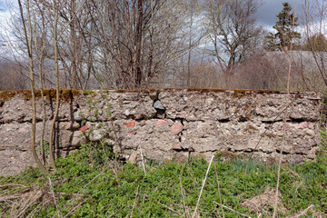 Old cracked concrete house foundation with big and small rocks, bricks and moss