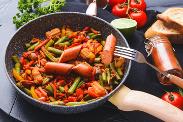 Frying pan with tasty sausage and vegetables on dark wooden background, closeup