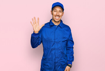 Bald man with beard wearing builder jumpsuit uniform showing and pointing up with fingers number five while smiling confident and happy.