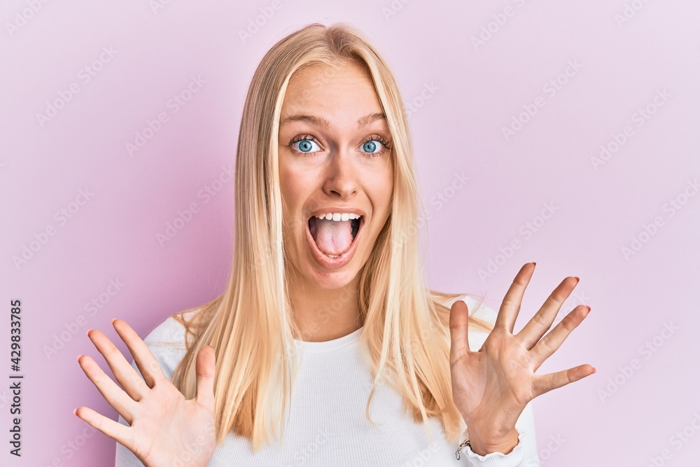 Poster young blonde girl wearing casual clothes celebrating crazy and amazed for success with arms raised a