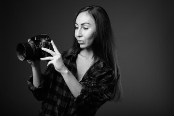 Studio shot of young beautiful hipster woman with camera in black and white