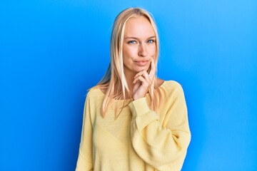 Young blonde girl wearing casual clothes thinking concentrated about doubt with finger on chin and...