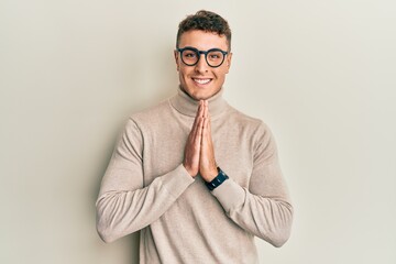 Hispanic young man wearing casual turtleneck sweater praying with hands together asking for...
