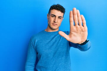 Hispanic young man wearing casual winter sweater doing stop sing with palm of the hand. warning...