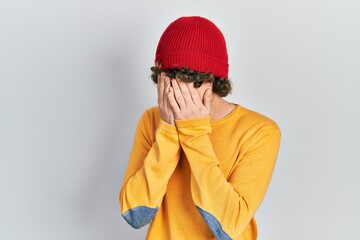 Handsome young man wearing wool hat with sad expression covering face with hands while crying. depression concept.