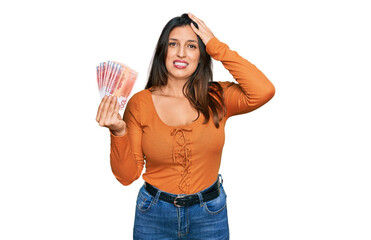 Beautiful hispanic woman holding norwegian krone banknotes stressed and frustrated with hand on...