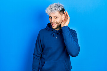 Fototapeta na wymiar Young hispanic man with modern dyed hair wearing casual blue sweatshirt smiling with hand over ear listening and hearing to rumor or gossip. deafness concept.