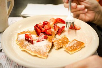 A patron at a diner finishes her pancakes with fresh strawberries and granulated sugar.