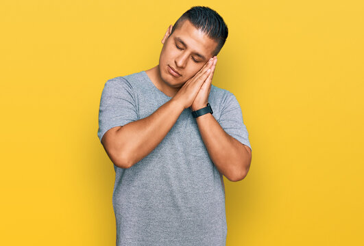 Young latin man wearing casual clothes sleeping tired dreaming and posing with hands together while smiling with closed eyes.