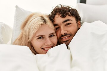Young beautiful couple lying in bed and covering with blanket at home.