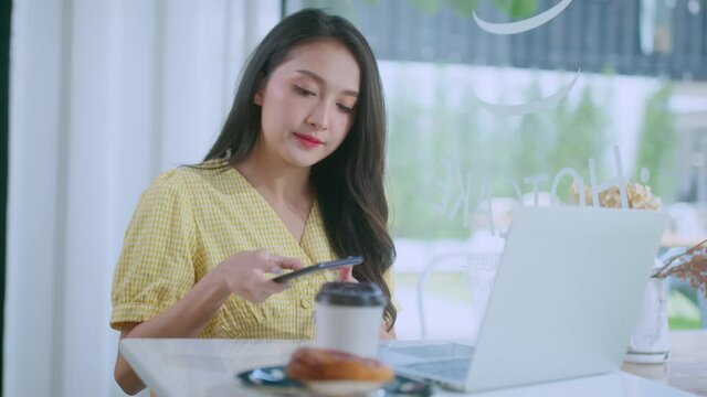 young attractive asian female wear casual cloth hand use smartphone and laptop device comminication social contact in cafe restaruant sit at counter next to big window daylight