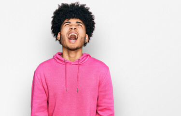 Young african american man with afro hair wearing casual pink sweatshirt angry and mad screaming frustrated and furious, shouting with anger. rage and aggressive concept.