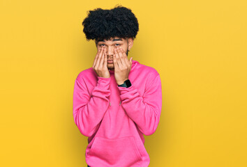 Young african american man with afro hair wearing casual pink sweatshirt rubbing eyes for fatigue...