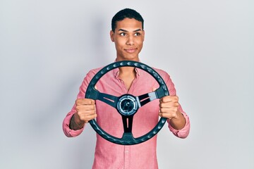 Young african american guy holding steering wheel smiling looking to the side and staring away thinking.