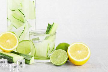 cucumber water in a bottle and glass with lime and lemon on a gray background, detox