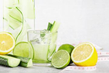 cucumber water in a bottle and glass with lime and lemon on a gray background, detox, tape for measurements, diet