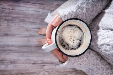 A comforting cup of coffee in the hands of a woman with a big, cosy jumper
