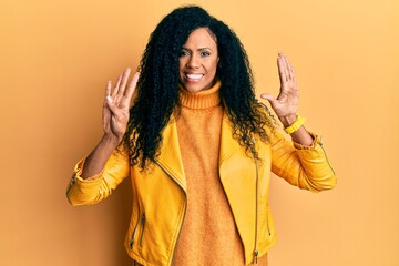 Middle age african american woman wearing wool winter sweater and leather jacket showing and pointing up with fingers number nine while smiling confident and happy.