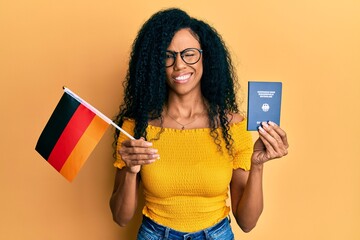 Middle age african american woman holding germany flag and passport winking looking at the camera...