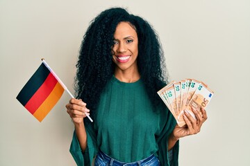 Middle age african american woman holding germany flag and euros banknotes smiling with a happy and cool smile on face. showing teeth.