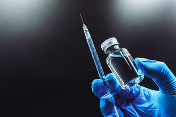 The vaccine concept is in the hands of a doctor's white vaccine bottle and a blue glove with copy space, isolated on black background