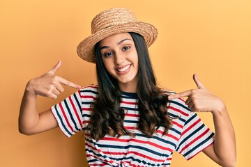 Young hispanic woman wearing summer hat looking confident with smile on face, pointing oneself with fingers proud and happy.