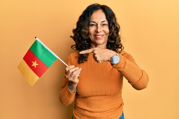 Middle age hispanic woman holding cameroon flag smiling happy pointing with hand and finger