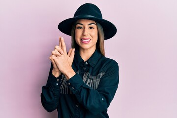 Fototapeta premium Young hispanic woman wearing cowgirl style doing pistol gesture with hands smiling with a happy and cool smile on face. showing teeth.
